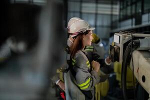 ingenieros cheque controlar pesado máquina robot brazo. diverso equipo de industrial robótica ingenieros reunido alrededor máquina. profesional maquinaria operadores reparar eléctrico robot en brillante digital panel. foto