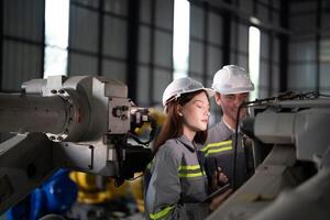 engineers check control heavy machine robot arm. Diverse Team of Industrial Robotics Engineers Gathered Around Machine. Professional Machinery Operators repair electric robot on bright digital panel. photo