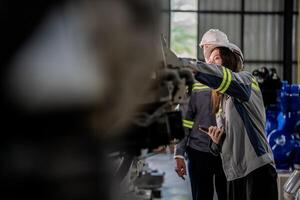 Factory engineer woman inspecting on machine with smart tablet. Worker works at machine robot arm. The welding machine with a remote system in an industrial factory. Artificial intelligence concept. photo