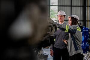 Factory engineer woman inspecting on machine with smart tablet. Worker works at machine robot arm. The welding machine with a remote system in an industrial factory. Artificial intelligence concept. photo