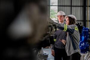 Factory engineer woman inspecting on machine with smart tablet. Worker works at machine robot arm. The welding machine with a remote system in an industrial factory. Artificial intelligence concept. photo