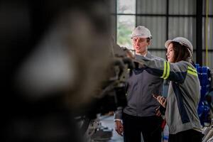 fábrica ingeniero mujer inspeccionando en máquina con inteligente tableta. trabajador trabajos a máquina robot brazo. el soldadura máquina con un remoto sistema en un industrial fábrica. artificial inteligencia concepto. foto