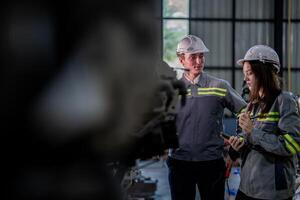 fábrica ingeniero mujer inspeccionando en máquina con inteligente tableta. trabajador trabajos a máquina robot brazo. el soldadura máquina con un remoto sistema en un industrial fábrica. artificial inteligencia concepto. foto