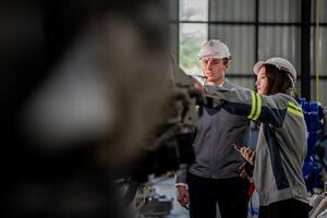 Factory engineer woman inspecting on machine with smart tablet. Worker works at machine robot arm. The welding machine with a remote system in an industrial factory. Artificial intelligence concept. photo