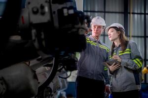 Factory engineer woman inspecting on machine with smart tablet. Worker works at machine robot arm. The welding machine with a remote system in an industrial factory. Artificial intelligence concept. photo