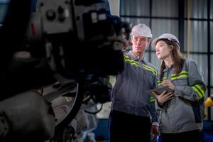 fábrica ingeniero mujer inspeccionando en máquina con inteligente tableta. trabajador trabajos a máquina robot brazo. el soldadura máquina con un remoto sistema en un industrial fábrica. artificial inteligencia concepto. foto