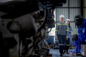 Factory engineer woman inspecting on machine with smart tablet. Worker works at machine robot arm. The welding machine with a remote system in an industrial factory. Artificial intelligence concept. photo