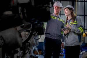 Factory engineer woman inspecting on machine with smart tablet. Worker works at machine robot arm. The welding machine with a remote system in an industrial factory. Artificial intelligence concept. photo