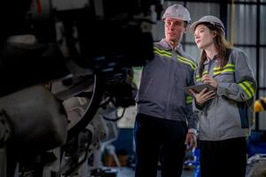 Factory engineer woman inspecting on machine with smart tablet. Worker works at machine robot arm. The welding machine with a remote system in an industrial factory. Artificial intelligence concept. photo