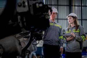 Factory engineer woman inspecting on machine with smart tablet. Worker works at machine robot arm. The welding machine with a remote system in an industrial factory. Artificial intelligence concept. photo