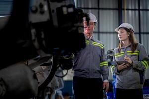 Factory engineer woman inspecting on machine with smart tablet. Worker works at machine robot arm. The welding machine with a remote system in an industrial factory. Artificial intelligence concept. photo