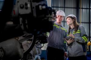 Factory engineer woman inspecting on machine with smart tablet. Worker works at machine robot arm. The welding machine with a remote system in an industrial factory. Artificial intelligence concept. photo