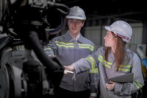 negocio ingenieros reunirse y cheque controlar pesado máquina robot brazo. diverso equipo de industrial robótica ingenieros reunido alrededor máquina. profesional maquinaria operador utilizar industrial digital tableta. foto