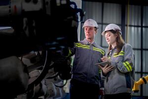 Factory engineer woman inspecting on machine with smart tablet. Worker works at machine robot arm. The welding machine with a remote system in an industrial factory. Artificial intelligence concept. photo