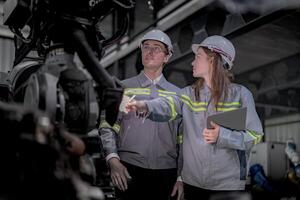Sales manager and factory owner in suits negotiating selling robots used in the factory. Business engineers meeting and checking new machine robot. Workers walking at warehouse welding machine. photo