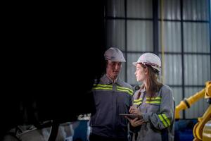 Factory engineer woman inspecting on machine with smart tablet. Worker works at machine robot arm. The welding machine with a remote system in an industrial factory. Artificial intelligence concept. photo