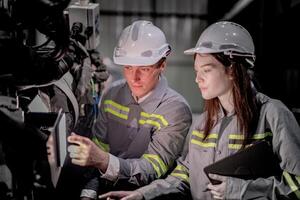 Business engineers meet and check control heavy machine robot arm. Diverse Team of Industrial Robotics Engineers Gathered Around machine. Professional Machinery Operator Use Industrial Digital Tablet. photo