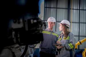 Factory engineer woman inspecting on machine with smart tablet. Worker works at machine robot arm. The welding machine with a remote system in an industrial factory. Artificial intelligence concept. photo