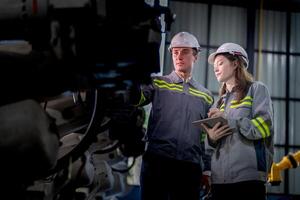 Factory engineer woman inspecting on machine with smart tablet. Worker works at machine robot arm. The welding machine with a remote system in an industrial factory. Artificial intelligence concept. photo