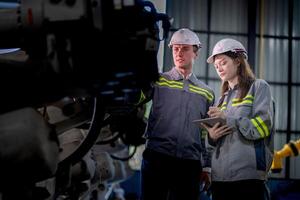 Factory engineer woman inspecting on machine with smart tablet. Worker works at machine robot arm. The welding machine with a remote system in an industrial factory. Artificial intelligence concept. photo