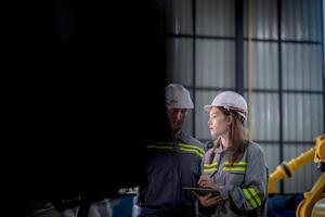 fábrica ingeniero mujer inspeccionando en máquina con inteligente tableta. trabajador trabajos a máquina robot brazo. el soldadura máquina con un remoto sistema en un industrial fábrica. artificial inteligencia concepto. foto