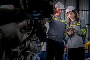 Factory engineer woman inspecting on machine with smart tablet. Worker works at machine robot arm. The welding machine with a remote system in an industrial factory. Artificial intelligence concept. photo