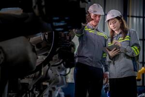 fábrica ingeniero mujer inspeccionando en máquina con inteligente tableta. trabajador trabajos a máquina robot brazo. el soldadura máquina con un remoto sistema en un industrial fábrica. artificial inteligencia concepto. foto