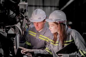 Sales manager and factory owner in suits negotiating selling robots used in the factory. Business engineers meeting and checking new machine robot. Workers walking at warehouse welding machine. photo