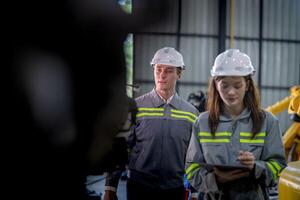 Factory engineer woman inspecting on machine with smart tablet. Worker works at machine robot arm. The welding machine with a remote system in an industrial factory. Artificial intelligence concept. photo