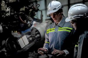 engineers check control heavy machine robot arm. Diverse Team of Industrial Robotics Engineers Gathered Around Machine. Professional Machinery Operators repair electric robot on bright digital panel. photo