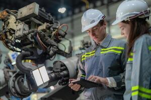 Factory engineer woman inspecting on machine with smart tablet. Worker works at machine robot arm. The welding machine with a remote system in an industrial factory. Artificial intelligence concept. photo