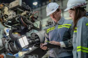 Factory engineer woman inspecting on machine with smart tablet. Worker works at machine robot arm. The welding machine with a remote system in an industrial factory. Artificial intelligence concept. photo