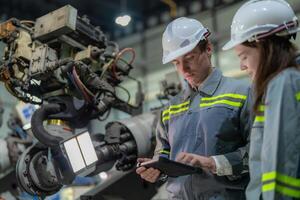 Factory engineer woman inspecting on machine with smart tablet. Worker works at machine robot arm. The welding machine with a remote system in an industrial factory. Artificial intelligence concept. photo