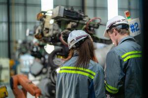 Factory engineer woman inspecting on machine with smart tablet. Worker works at machine robot arm. The welding machine with a remote system in an industrial factory. Artificial intelligence concept. photo