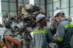 Factory engineer woman inspecting on machine with smart tablet. Worker works at machine robot arm. The welding machine with a remote system in an industrial factory. Artificial intelligence concept. photo