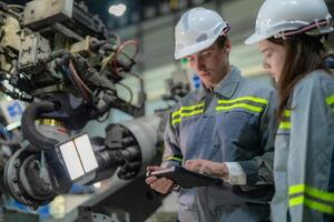 Factory engineer woman inspecting on machine with smart tablet. Worker works at machine robot arm. The welding machine with a remote system in an industrial factory. Artificial intelligence concept. photo