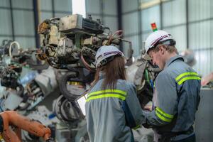 Factory engineer woman inspecting on machine with smart tablet. Worker works at machine robot arm. The welding machine with a remote system in an industrial factory. Artificial intelligence concept. photo