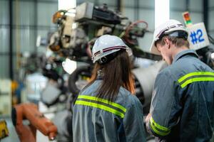 Factory engineer woman inspecting on machine with smart tablet. Worker works at machine robot arm. The welding machine with a remote system in an industrial factory. Artificial intelligence concept. photo