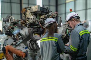 Factory engineer woman inspecting on machine with smart tablet. Worker works at machine robot arm. The welding machine with a remote system in an industrial factory. Artificial intelligence concept. photo