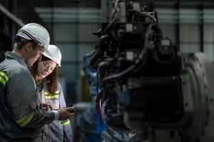 Factory engineer woman inspecting on machine with smart tablet. Worker works at machine robot arm. The welding machine with a remote system in an industrial factory. Artificial intelligence concept. photo