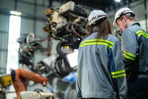 Factory engineer woman inspecting on machine with smart tablet. Worker works at machine robot arm. The welding machine with a remote system in an industrial factory. Artificial intelligence concept. photo