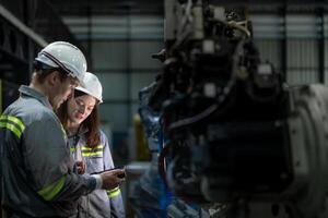 Factory engineer woman inspecting on machine with smart tablet. Worker works at machine robot arm. The welding machine with a remote system in an industrial factory. Artificial intelligence concept. photo