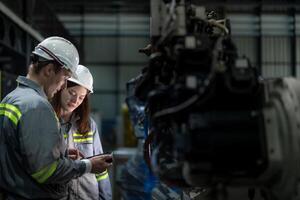 Factory engineer woman inspecting on machine with smart tablet. Worker works at machine robot arm. The welding machine with a remote system in an industrial factory. Artificial intelligence concept. photo