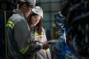 Factory engineer woman inspecting on machine with smart tablet. Worker works at machine robot arm. The welding machine with a remote system in an industrial factory. Artificial intelligence concept. photo