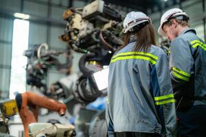 Factory engineer woman inspecting on machine with smart tablet. Worker works at machine robot arm. The welding machine with a remote system in an industrial factory. Artificial intelligence concept. photo