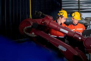 grupo de masculino ingeniero trabajadores mantenimiento automático robótico brazo máquina en un oscuro habitación fábrica. trabajador comprobación y reparando automático robot mano máquina. trabajador vistiendo la seguridad lentes y casco. foto