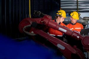 group of male engineer workers maintenance automatic robotic arm machine in a dark room factory. worker checking and repairing automatic robot hand machine. Worker wearing safety glasses and helmet. photo