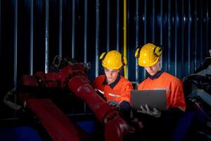 group of male engineer workers maintenance automatic robotic arm machine in a dark room factory. worker checking and repairing automatic robot hand machine. Worker wearing safety glasses and helmet. photo