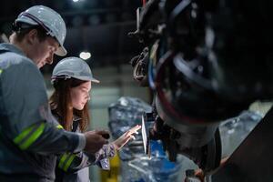 Factory engineer woman inspecting on machine with smart tablet. Worker works at machine robot arm. The welding machine with a remote system in an industrial factory. Artificial intelligence concept. photo