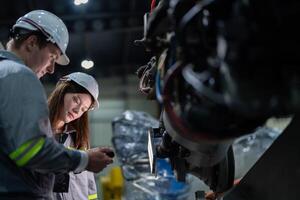 Factory engineer woman inspecting on machine with smart tablet. Worker works at machine robot arm. The welding machine with a remote system in an industrial factory. Artificial intelligence concept. photo